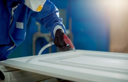 Close-up of worker spraying timber with spray gun and woodworking factory.