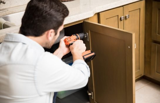 Point of view of a young handyman using a power drill to fix a door in a kitchen cabinet